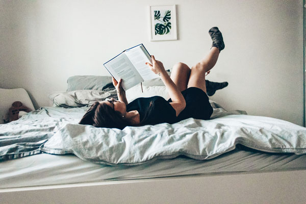 ベッドに寝そべって本を読む女性